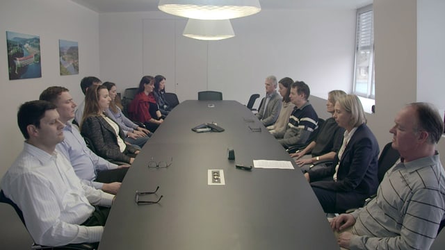 Rund ein Duzend Menschen sitzen mit geschlossenen Augen um einen ovalen Tisch. Rund ein Duzend Menschen sitzen mit geschlossenen Augen um einen ovalen Tisch.