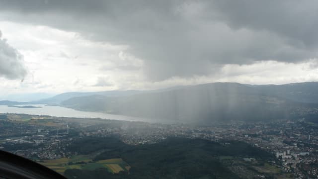 Flugbild: Landschaft mit See und Jurahügeln im Hintergrund. Im Vordergrund graue Wolke mit fallenden Regenstreifen. Flugbild: Landschaft mit See und Jurahügeln im Hintergrund. Im Vordergrund graue Wolke mit fallenden Regenstreifen.