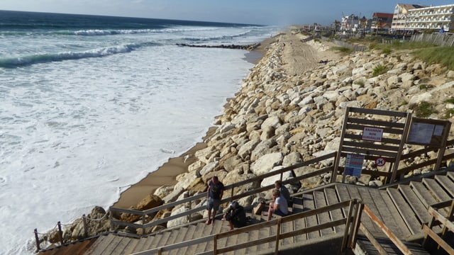 Ein Deich an einem Strand, der Ozean kommt immer näher Ein Deich an einem Strand, der Ozean kommt immer näher