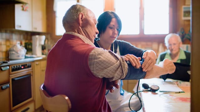Eine Spitexmitarbeiterin misst den Blutdruck eines Patienten Eine Spitexmitarbeiterin misst den Blutdruck eines Patienten