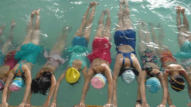 Mädchen beim Schwimmunterricht in bunten Schwimmanzügen im Wasser Mädchen beim Schwimmunterricht in bunten Schwimmanzügen im Wasser