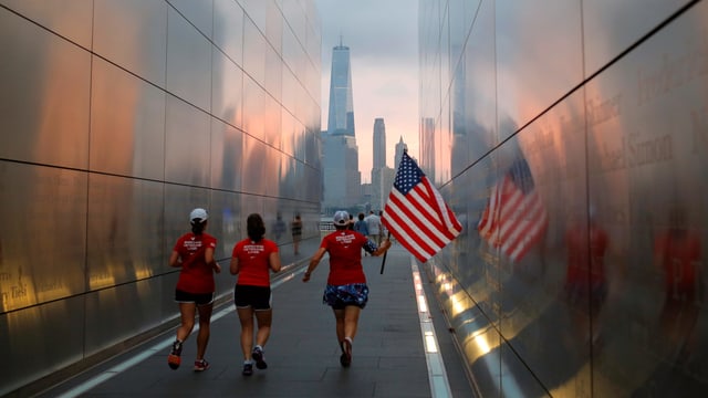Frauen, die mit einer amerikanischen Flagge durch das Memorial von 9/11 rennen. Frauen, die mit einer amerikanischen Flagge durch das Memorial von 9/11 rennen.