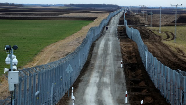 Eine Strasse. Rechts und links davon ein hoher Zaun. Eine Strasse. Rechts und links davon ein hoher Zaun.