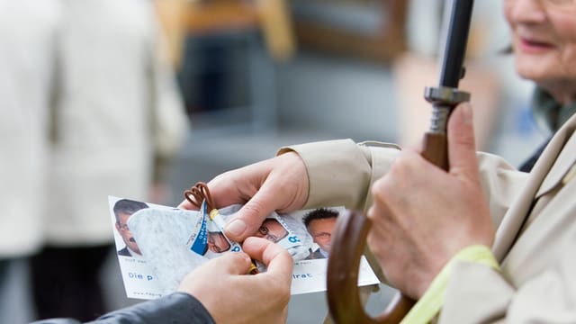Einer älteren Passantin werden Flyer und Schnürsenkel verteilt. Einer älteren Passantin werden Flyer und Schnürsenkel verteilt.