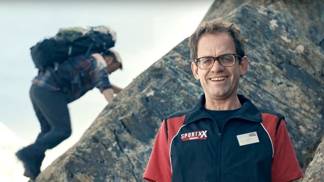 Ein Sportartikelverkäufer im Vordergrund, im Hintergrund ein Bergsteiger Ein Sportartikelverkäufer im Vordergrund, im Hintergrund ein Bergsteiger