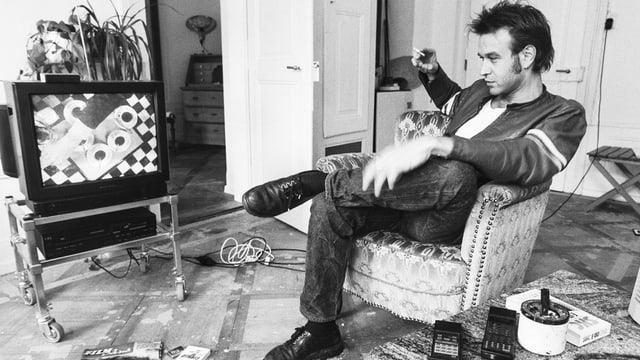 Wohnzimmer. Junger Mann flätzt auf Sofa und schaut TV. Wohnzimmer. Junger Mann flätzt auf Sofa und schaut TV.