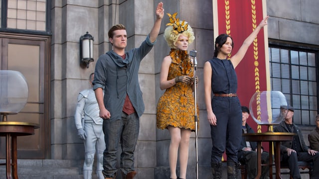 Szene aus Hunger Games, die beiden Hauptfiguren mit erhobenem linken Arm. Szene aus Hunger Games, die beiden Hauptfiguren mit erhobenem linken Arm.