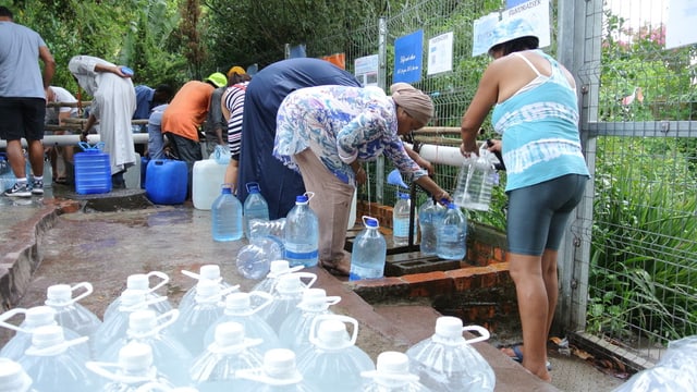 Personen füllen Wasserflaschen und -kanister mit Wasser. Personen füllen Wasserflaschen und -kanister mit Wasser.