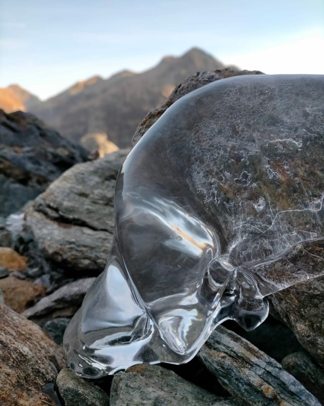 Blasenartige Eisformation auf einem Fels, dahinter Berge zu sehen