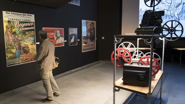 Ein Mann steht vor einem Filmplakat. Er steht in einem Ausstellungsraum. Ein Mann steht vor einem Filmplakat. Er steht in einem Ausstellungsraum.