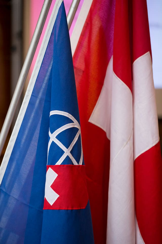 Schweizer Flagge, daneben eine blaue Fahne mit Weltkugel und kleinem Schweizer Kreuz. Schweizer Flagge, daneben eine blaue Fahne mit Weltkugel und kleinem Schweizer Kreuz.