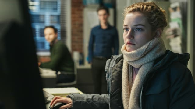 Eine Frau sitzt an einem Bürotisch, im Hintergrund schauen ihr zwei Männer zu Eine Frau sitzt an einem Bürotisch, im Hintergrund schauen ihr zwei Männer zu