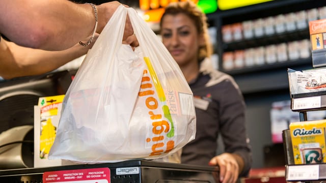 Hand einer Kundin in einem Tankstellenshop nimmt einen Plastiksack von der Kassentheke Hand einer Kundin in einem Tankstellenshop nimmt einen Plastiksack von der Kassentheke