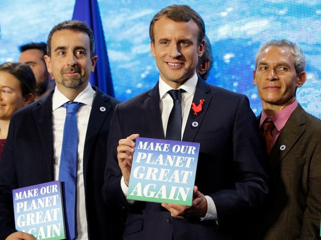 Macron mit einem Poster in der Hand. Macron mit einem Poster in der Hand.