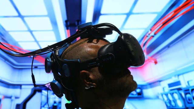 Ein Mann sitzt unter einer VR-Brille. Ein Mann sitzt unter einer VR-Brille.