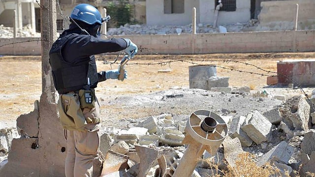 Ein Man mit Helm und Gasmaske füllt eine Probe in einen Behälter ab. Ein Man mit Helm und Gasmaske füllt eine Probe in einen Behälter ab.