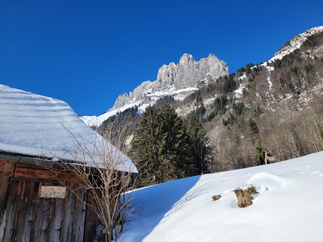 Verschneite Scheune vor Bergkulisse.