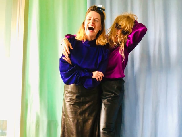 Zwei Frauen in bunter Kleidung vor einem blauen und einem grünen Aushang Zwei Frauen in bunter Kleidung vor einem blauen und einem grünen Aushang