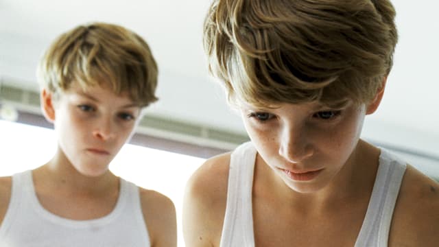 Zwei Jungen in weissen Unterhemden, konzentriert nach unten blickend. Zwei Jungen in weissen Unterhemden, konzentriert nach unten blickend.