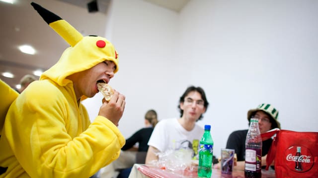 Ein junger Mann im Pikachu-Kostüm beisst in einen Hamburger. Ein junger Mann im Pikachu-Kostüm beisst in einen Hamburger.