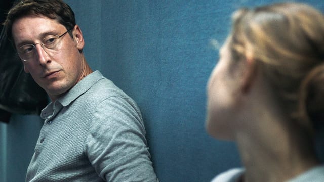Ein Mann mit Brille schaut eine Frau an, sie beide lehnen an einer Wand. Ein Mann mit Brille schaut eine Frau an, sie beide lehnen an einer Wand.