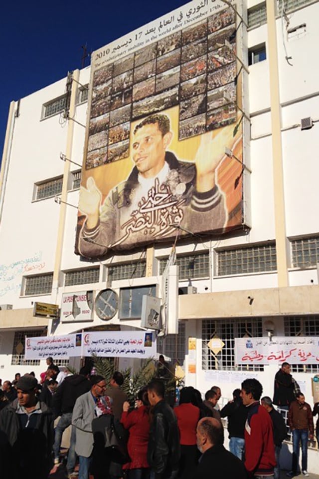 An einer Häuserwand ein grosses Plakat mit einem jungen Mann. An einer Häuserwand ein grosses Plakat mit einem jungen Mann.