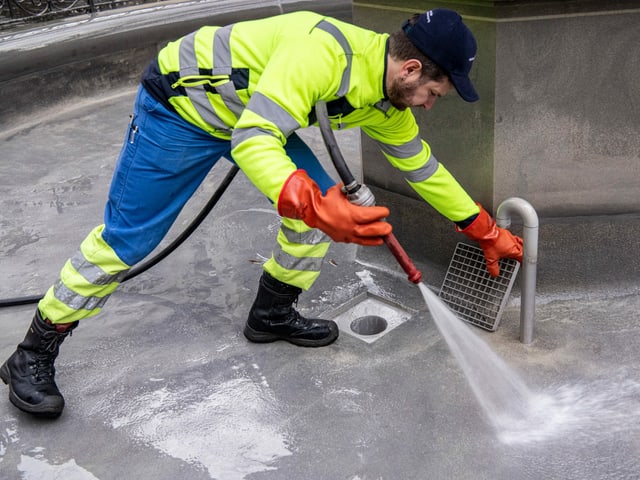 Brunnenwärter reinigt mit Schlauch einen Brunnen Brunnenwärter reinigt mit Schlauch einen Brunnen