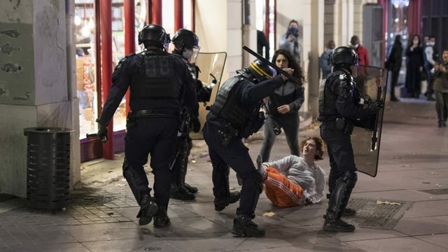 Four policemen are on the street, one beats a passerby with a truncheon.