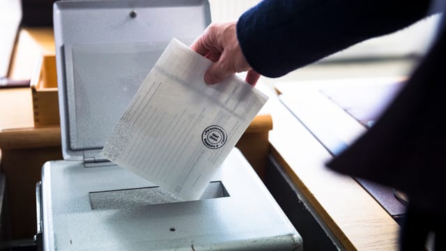 Eien Person legt einen Wahlzettel in die Urne. Eien Person legt einen Wahlzettel in die Urne.