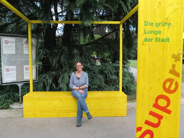 Pascale Contesse sitzt in einem gelben Holzkonstrukt auf einer Bank. Pascale Contesse sitzt in einem gelben Holzkonstrukt auf einer Bank.