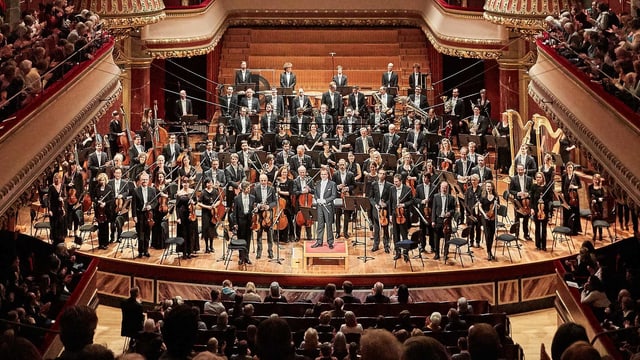 Ein Orchester steht auf einer Bühne. Ein Orchester steht auf einer Bühne.