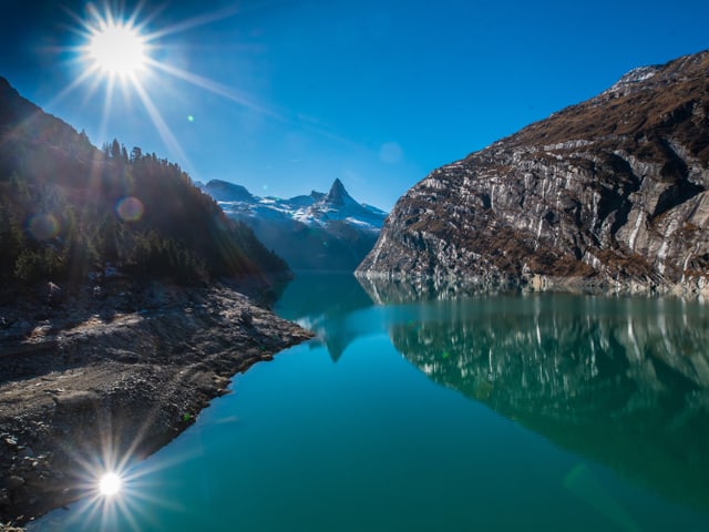 Der Zevreilasee in seinen tiefen Blautönen. Die Sonne spiegelt sich im See.