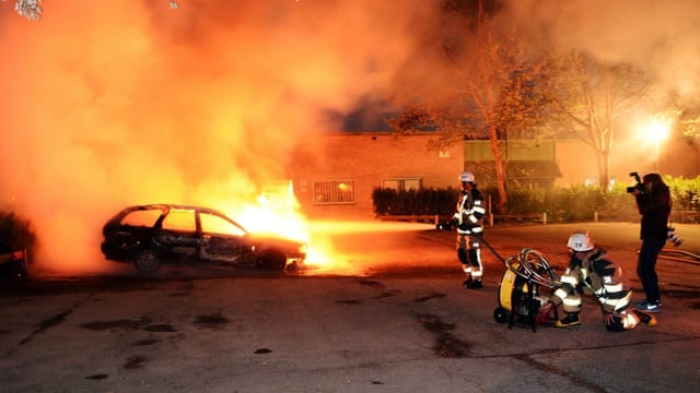 Feuerwehrmänner löschen ein brennendes Auto in Stockholm. Feuerwehrmänner löschen ein brennendes Auto in Stockholm.