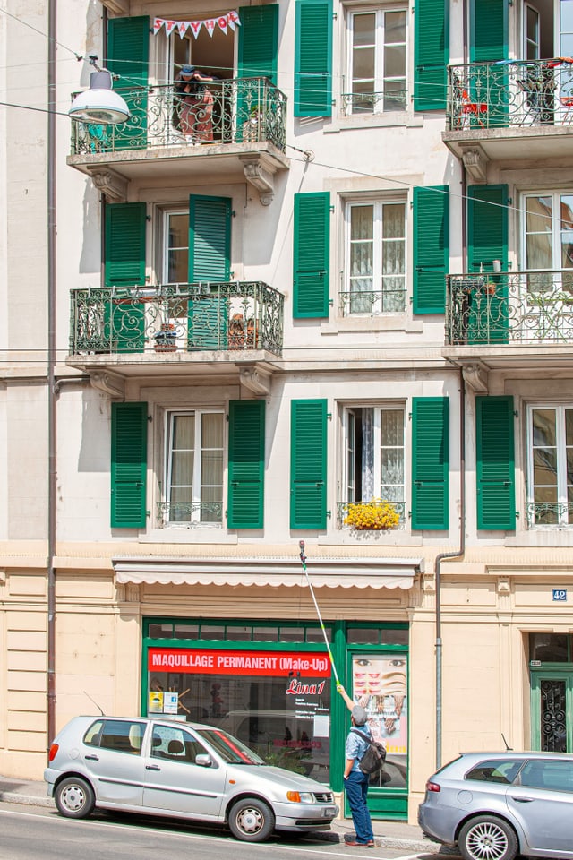 Ein Mann steht auf einer Strasse und streckt ein Teleskop-Mikrophon in Richtung einer Frau auf einem Balkon im zweiten Stock. Ein Mann steht auf einer Strasse und streckt ein Teleskop-Mikrophon in Richtung einer Frau auf einem Balkon im zweiten Stock.