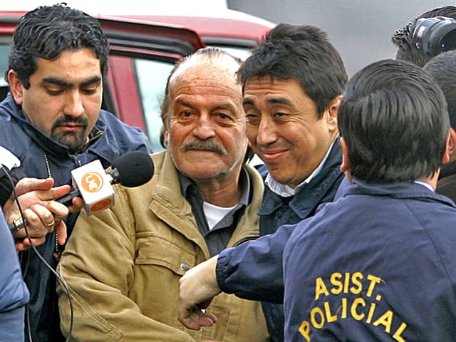 2007: Ex-General Raul Iturriaga ist in Santiago, Chile, von Polizisten umringt. Ein Journalist hält ihm ein Mikrophon vor den Mund. 2007: Ex-General Raul Iturriaga ist in Santiago, Chile, von Polizisten umringt. Ein Journalist hält ihm ein Mikrophon vor den Mund.