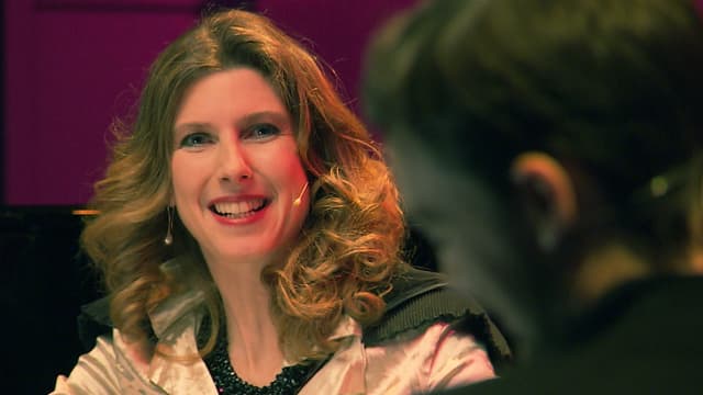 Eine Frau mit blondem Haar, schwarzer Halskette und weissem Mini-Mikrophon. das kaum von einem Ohrring zu unterscheiden ist. Eine Frau mit blondem Haar, schwarzer Halskette und weissem Mini-Mikrophon. das kaum von einem Ohrring zu unterscheiden ist.
