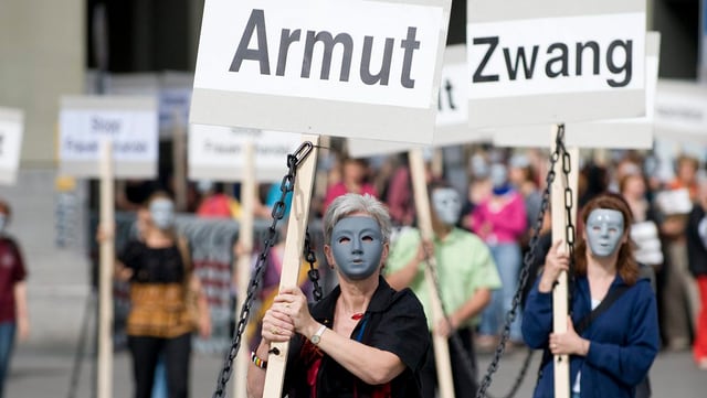 Frauen mit Masken im Gesicht tragen Plakate durch die Strasse. Auf denen steht: «Armut» und «Zwang». Frauen mit Masken im Gesicht tragen Plakate durch die Strasse. Auf denen steht: «Armut» und «Zwang».