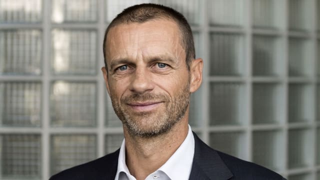 Ein junger Mann mit kurzem Haar und Dreitagebart vor einer Wand aus Glasziegeln. Ein junger Mann mit kurzem Haar und Dreitagebart vor einer Wand aus Glasziegeln.