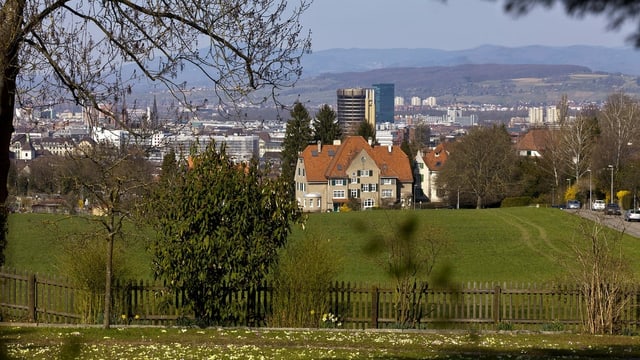 Im Vordergrund sieht man eine Wiese und einen Zaun, im Hintergrund ragt die Stadt empor. Im Vordergrund sieht man eine Wiese und einen Zaun, im Hintergrund ragt die Stadt empor.