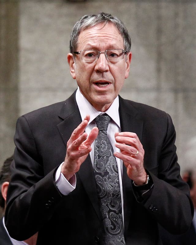 Cotler in Anzug und Krawatte mit Brille spricht und gestikuliert. Cotler in Anzug und Krawatte mit Brille spricht und gestikuliert.