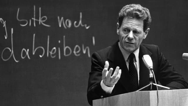 Mann in Anzug und Krawatte steht an einem Rednerpult, auf der Tafel im Hintergrund lässt sich der Schriftzug «Küng, bitte noch dableiben!» erahnen Mann in Anzug und Krawatte steht an einem Rednerpult, auf der Tafel im Hintergrund lässt sich der Schriftzug «Küng, bitte noch dableiben!» erahnen