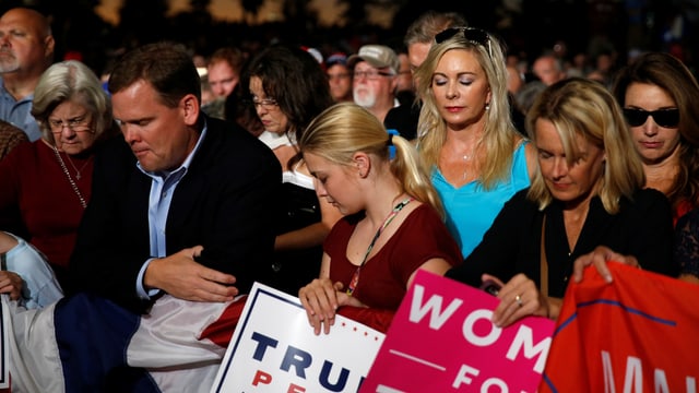 Eine Gruppe Frauen und Männer hält Trum Schilder und betet. Eine Gruppe Frauen und Männer hält Trum Schilder und betet.