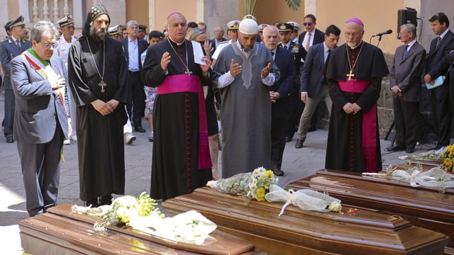 Ein römisch-katholischer Pfarrer, ein Pope und ein Imam segnen die Särge. Ein römisch-katholischer Pfarrer, ein Pope und ein Imam segnen die Särge.