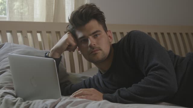 Mann mit Stubel-Frise auf Bett am chillen. Hat einen Laptop vor sich. Mann mit Stubel-Frise auf Bett am chillen. Hat einen Laptop vor sich.