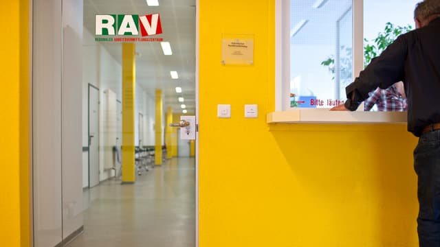 Ein Mann von hinten am Schalter einer RAV-Stelle. Ein Mann von hinten am Schalter einer RAV-Stelle.