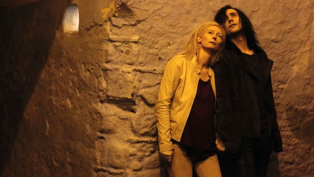 Tilda Swinton als Eve und Tom Hiddleston als Adam, zusammen an einer gruftartigen Wand gelehnt, nach oben blickend. Tilda Swinton als Eve und Tom Hiddleston als Adam, zusammen an einer gruftartigen Wand gelehnt, nach oben blickend.