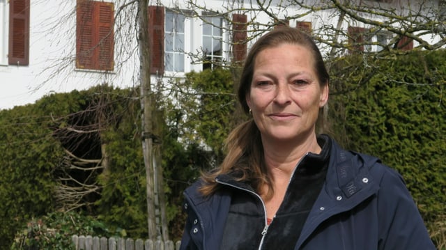 Eine Frau in blauer Jacke steht vor einer Hecke. Eine Frau in blauer Jacke steht vor einer Hecke.