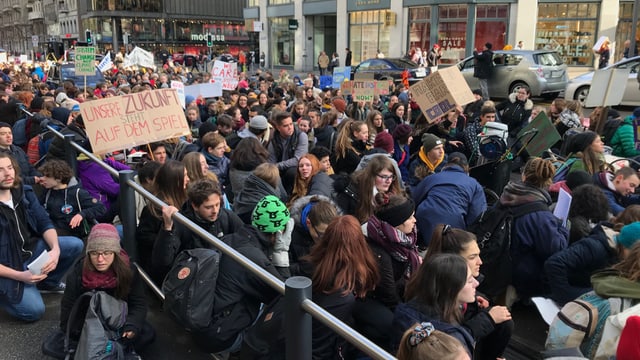 Eine Gruppe von Schülerinnen und Schülern sitzt auf der Bahnhofstrasse. Eine Gruppe von Schülerinnen und Schülern sitzt auf der Bahnhofstrasse.