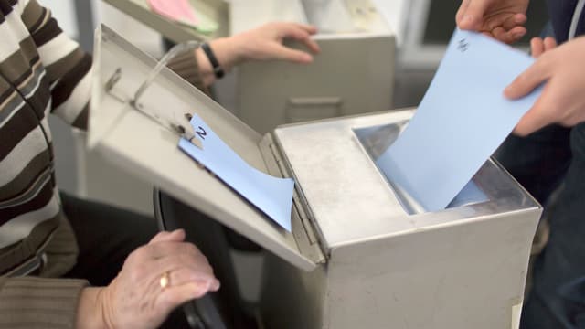 Eine Person wirft einen Stimmzettel in eine Wahlurne Eine Person wirft einen Stimmzettel in eine Wahlurne