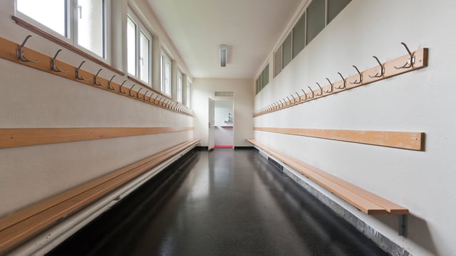 Ein leeres Schulhaus von Innen. An den Wänden auf beiden Seiten sind Bänke und Kleiderhacken angebracht. Ein leeres Schulhaus von Innen. An den Wänden auf beiden Seiten sind Bänke und Kleiderhacken angebracht.